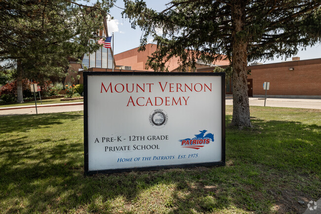 A sign under a tree on the green grass at Mount Vernon Academy.l