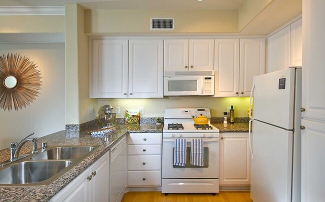 Classic Package I kitchen with white appliances, beige speckled granite countertop, white cabinetry, and hard surface flooring