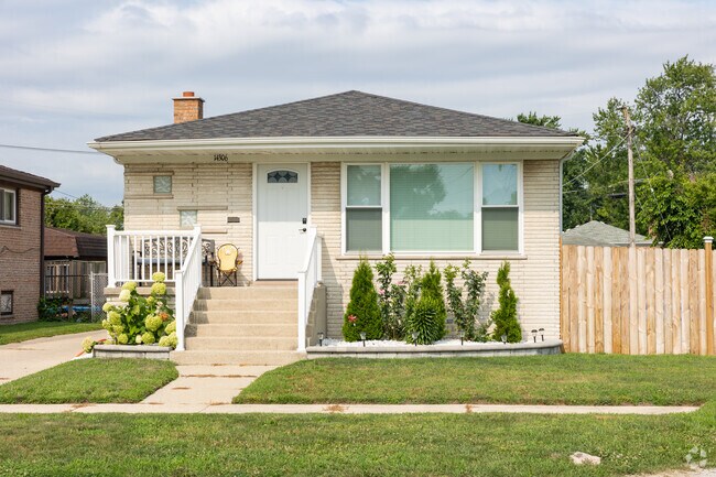 White brick ranch style home with large bay window, green lawn and flowers, Burnham, IL.