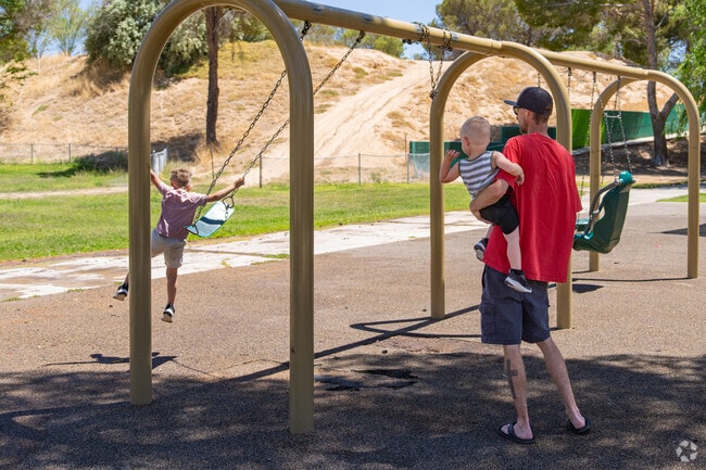 A young father holds his son while his brother jumps off the swing at Central Park.