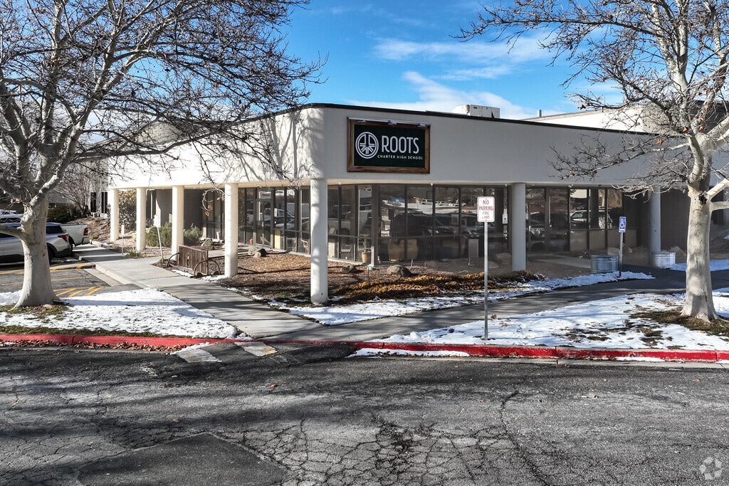 Roots Charter High School has a white facade flanked by mature trees.