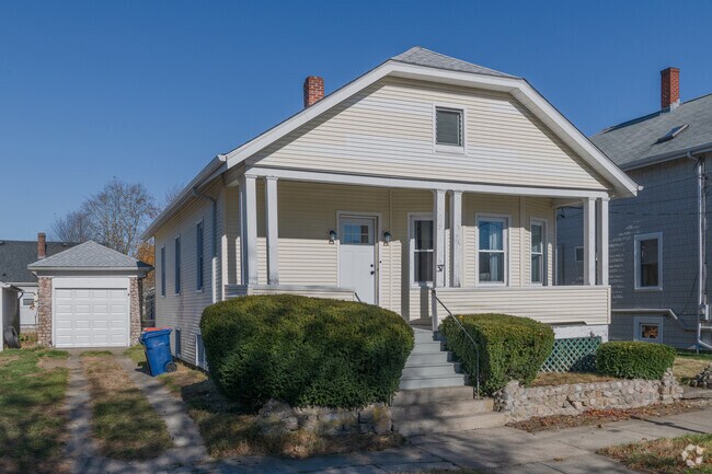 A modest bungalow in the Acushnet / Pine Hill neighborhood has a garage and a cobblestone fence.