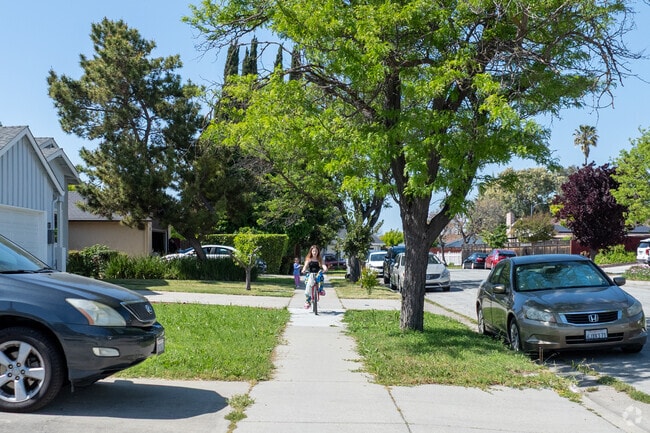 Kids ride bikes and play under shady trees along a quiet residential sidewalk in Vinci South.