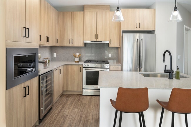 Signature Collection kitchen with stainless steel appliances (wine fridge included), quartz countertops, quartz tile backsplash, oak cabinetry, and hard-surface flooring