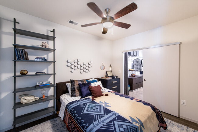 Bedroom with hard surface flooring, ceiling fan and barn door to customizable closet