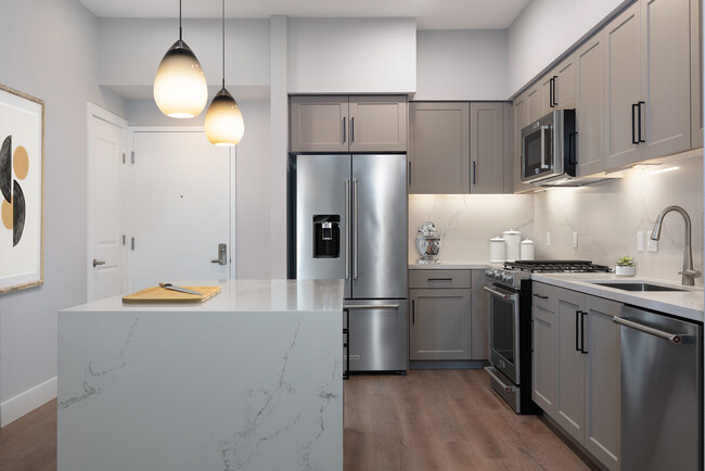 Signature Collection kitchen with upgraded stainless steel appliances, grey cabinetry, white marble countertops and backsplash, and hard surface flooring