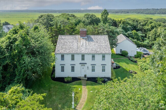A brilliant historic colonial is surrounded by lush trees in West Barnstable.