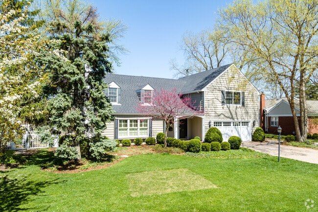 Cape Cod style home in neutral color scheme with blooming red bud tree in Ridgewood.