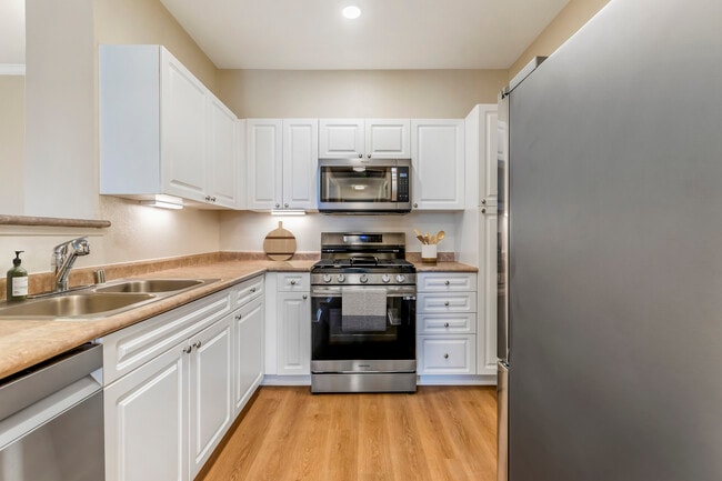 Classic Package II kitchen with upgraded stainless steel appliances, white cabinetry, neutral laminate countertops, and upgraded hard surface flooring