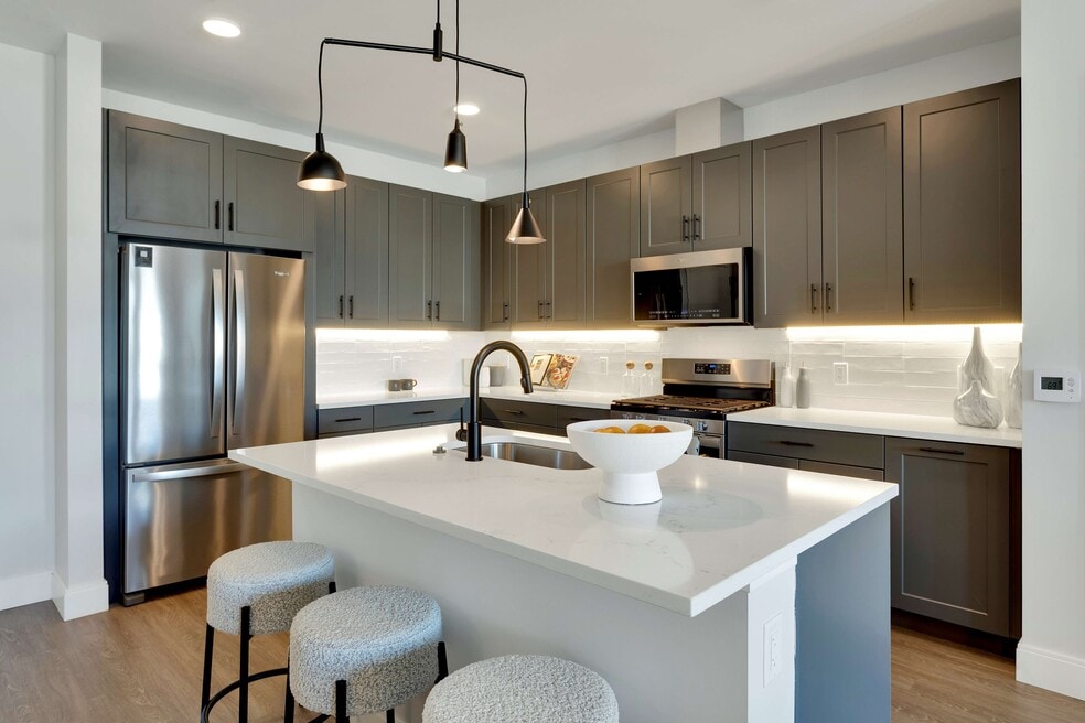 Modern kitchen with sleek dark cabinets, stainless steel appliances, and a stylish island featuring cozy stools and elegant lighting.