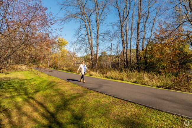 A woman walks down a paved path that winds along the Lamoille River in Fairfax Village.