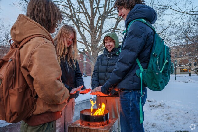 Students from the University of Vermont stay warm by the fire pits along the Andrew Harris Commons near Centennial.
