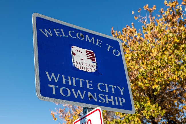 A blue sign welcoming people to White City Township stands out agains yellow leaves.