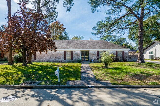 A single story home sits underneath mature trees in Baytown, Texas.