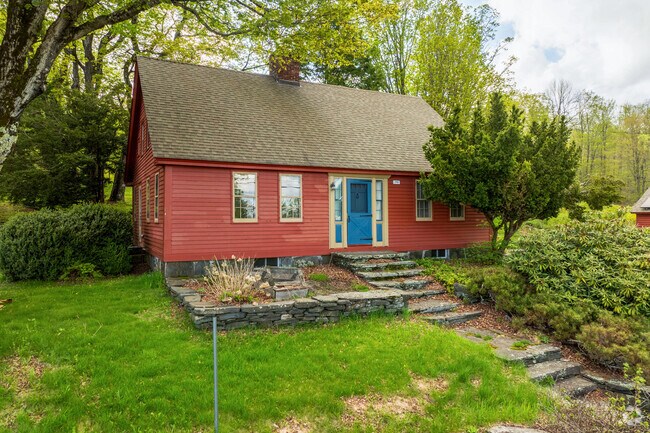A red clapboard sided home in Plainfield has a blue door and muted yellow trim accents.
