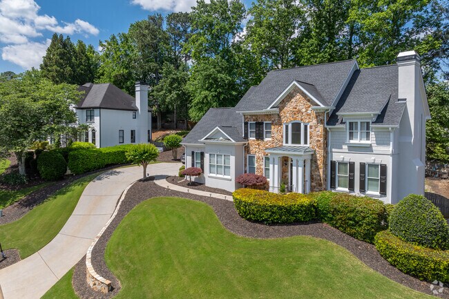 Traditional two-story homes in Medlock Bridge showcase a combination of stone and siding, accompanied by manicured landscaping and long driveways.