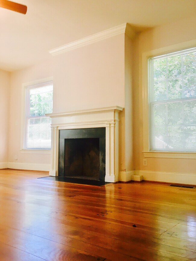 Living area with high ceilings, hardwood floors, and bright windows facing greenery.