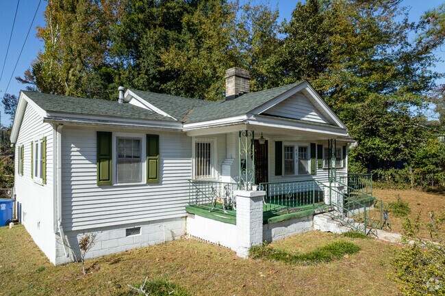 This white bungalow home in Burton Heights has a large front porch and is surrounded by trees.