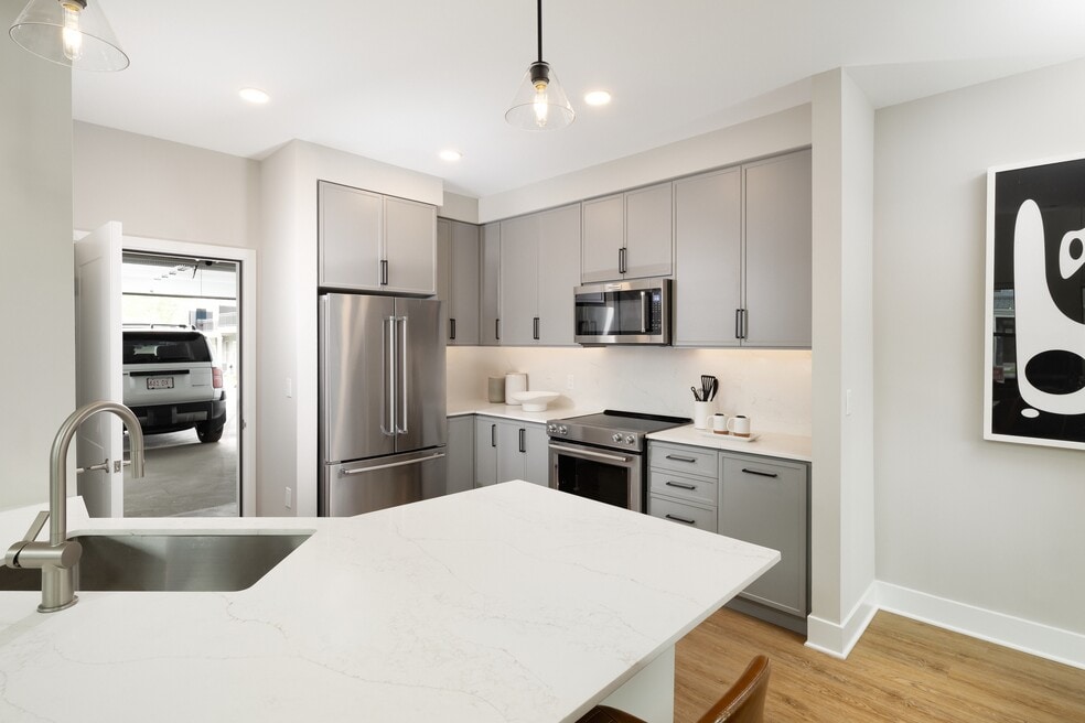 Signature Collection Townhome kitchen with upgraded stainless steel appliances, white quartz countertops and backsplash, grey cabinetry, hard surface flooring, and attached garage.