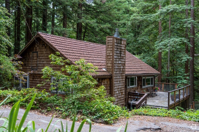 This craftsman-style cabin in Felton features a wood-shingled exterior and tile roof, blending seamlessly with the redwoods on a secluded, forested lot.