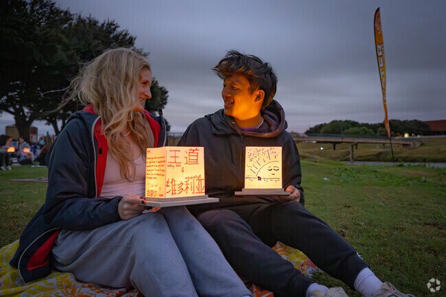 Friends hold illuminated lanterns, enjoying a magical night together by the Fort Worth river.