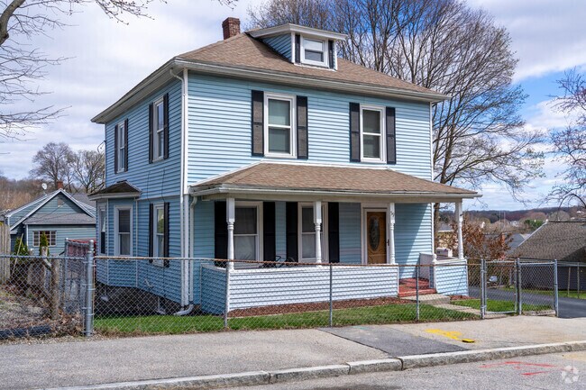 A single family foursquare style home in Hamilton has blue vinyl siding, black shutters and a front porch.