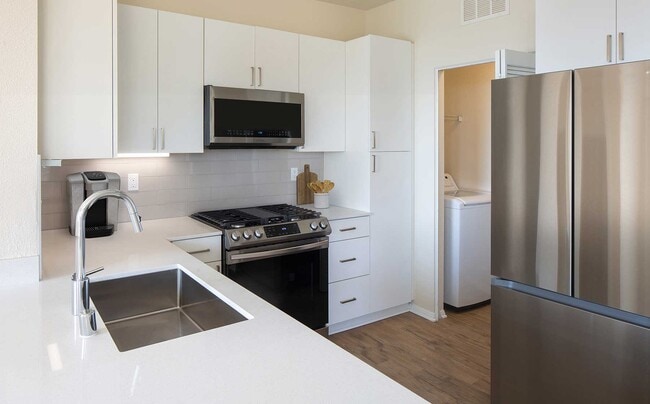 Renovated Package I kitchen featuring white cabinetry, white quartz countertops, stainless steel appliances, and hard surface flooring. In-unit laundry with full sized washer and dryer