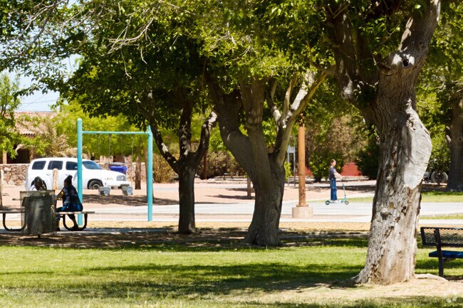 Kids ride scooters through Mesilla Park near the shaded gazebo.