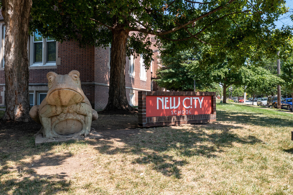A large frog statue sits next to the entrance of the New City School.