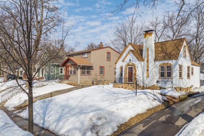 A Tudor Revival house with white stucco and accented stones on the corner of a block.