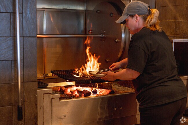 An employee at the Casa Grille Italiano cooks a steak over an open flame, near Cambridge Oaks.