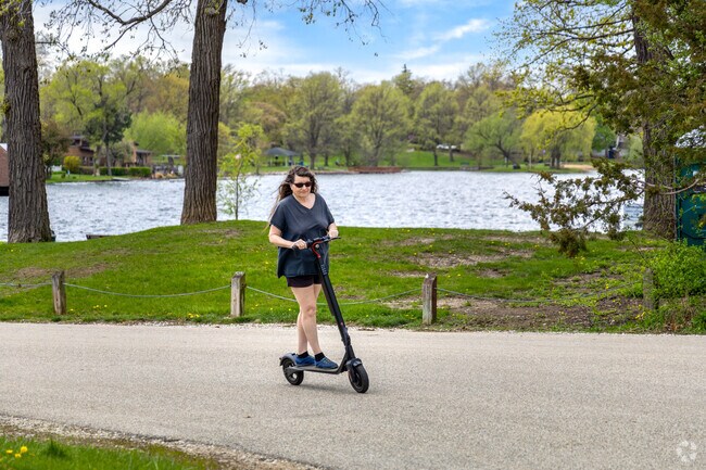 A woman rides a scooter by Sunset Beach with views of Gages Lake in the background.