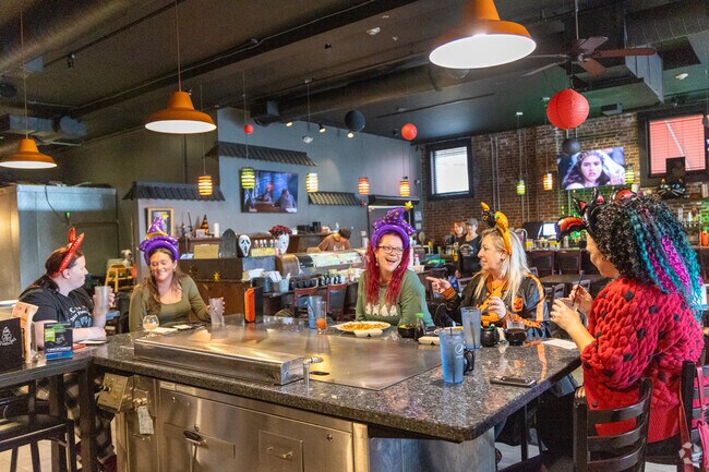 Friends share laughs and festive drinks inside a Salem restaurant, celebrating Halloween season with colorful costumes and lively conversation in the Witch City.