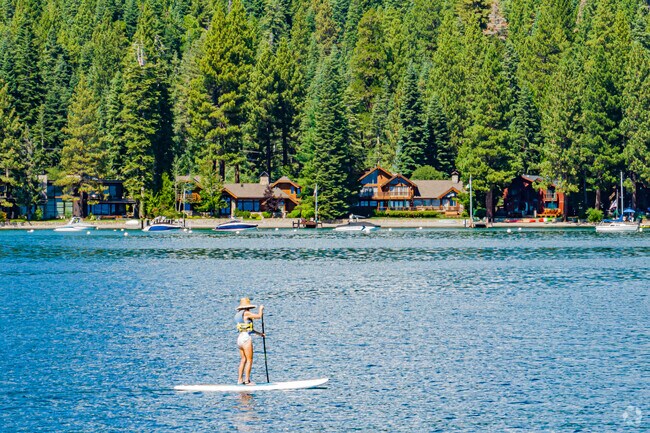 A woman paddle boards across Lake Tahoe in front of the beautiful homes of Carnelian Bay.