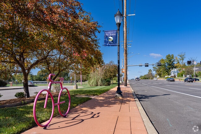 An artistic bicycle sculpture and City of St. John banner along St. Charles Rock Road.