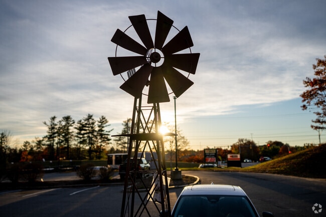 The evening sun sets behind a rustic windmill in Rindge, New Hampshire, casting warm light across the quiet roadside.