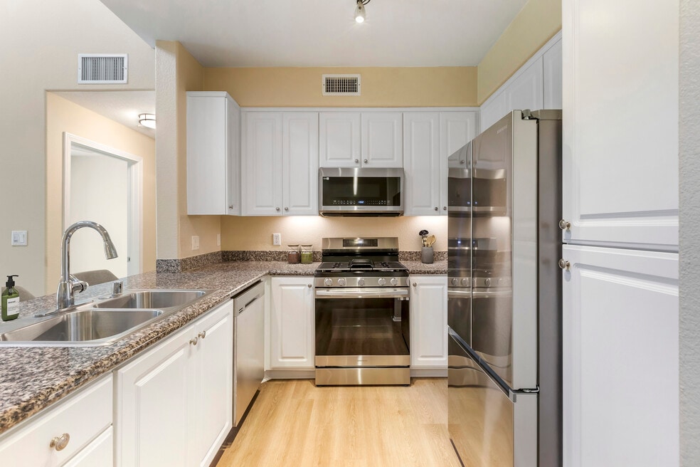 Renovated Package I kitchen with stainless steel appliances, beige speckled granite countertop, white cabinetry, and hard surface flooring