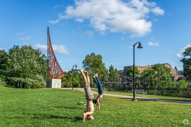 Folks do head stands on the green in front of a vertical art piece near South End.