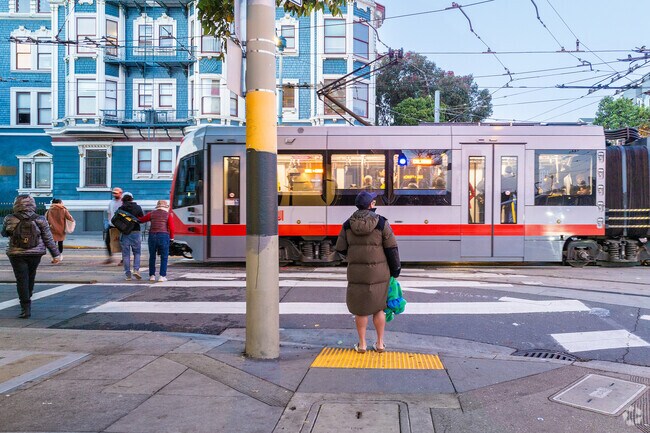 A woman waits to cross the street as a MUNI train goes by in Duboce Triangle.