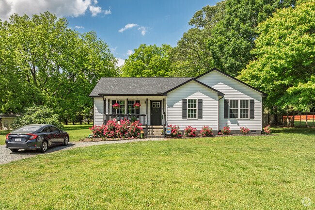 A cozy Liberty cottage is framed with blooming roses and shady mature trees.