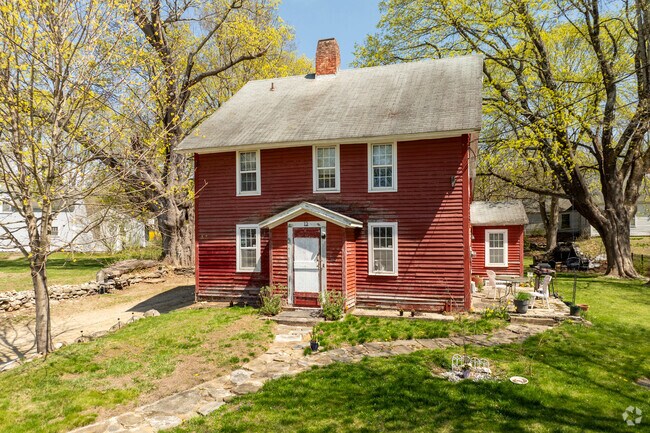 A colonial-style home in Scotland sits among trees, with red clapboard siding and white windows.