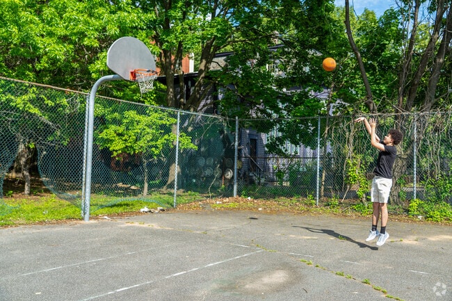 A person plays basketball on a court tucked within the greenery of Maple-High Six Corners.