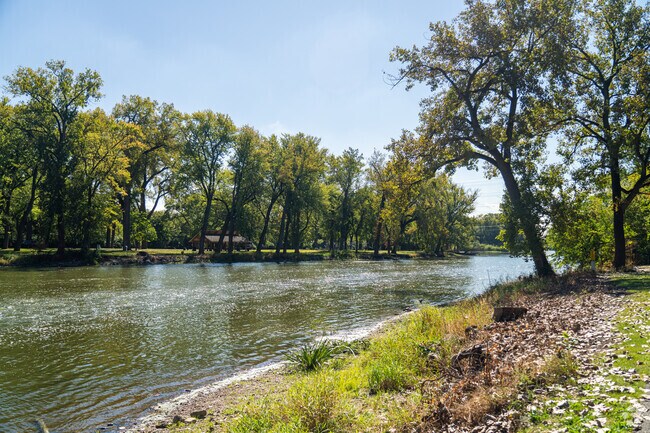 Mature trees line the bank of the river in Pigeon Hill's Fox River Trail Park in Aurora, IL.
