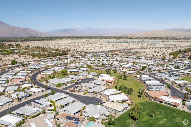 Aerial view of Palm Desert Greens Country Club shows fairways, pools, and desert backdrop.