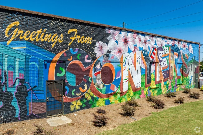 The 'Greetings From Conyers' mural is located in Olde Town Conyers next to the pavilion.