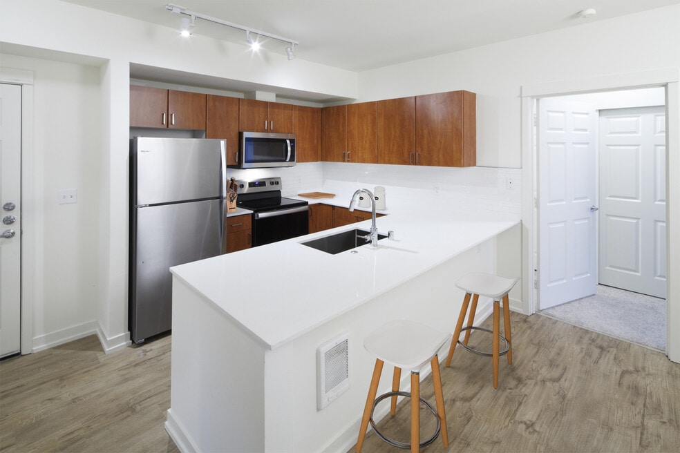 Renovated Package I kitchen with white quartz countertops, oak cabinetry, stainless steel appliances, tile backsplash, and hard surface flooring
