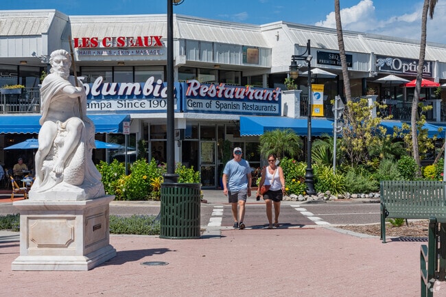 Locals stroll through a vibrant plaza near El Conquistador filled with shops and greenery.