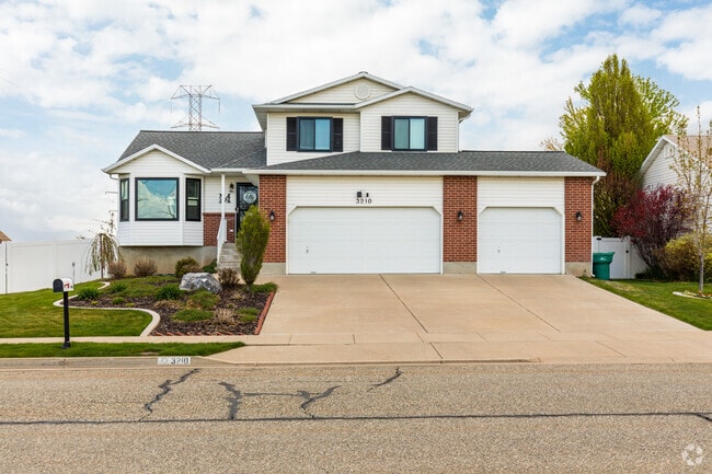 A charming home in Roy with a white stucco exterior and red brick accents, with a sloped roof and a well-maintained lawn.