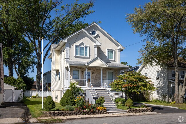 A raised mid-century colonial home in Little Ferry, NJ with colorful flowers in the front yard.