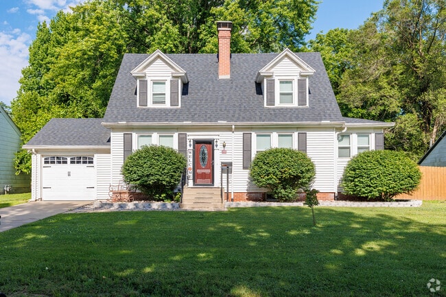A stately cape cod style home sits with a backdrop of large trees in Oak Grove.